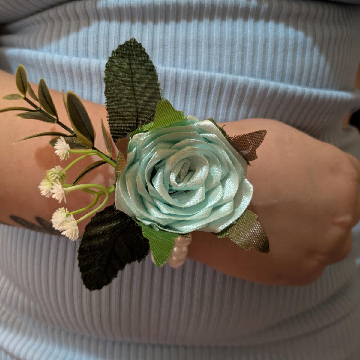 Aqua satin rose wrist corsage worn on wrist with pearl wristband and decorative greenery