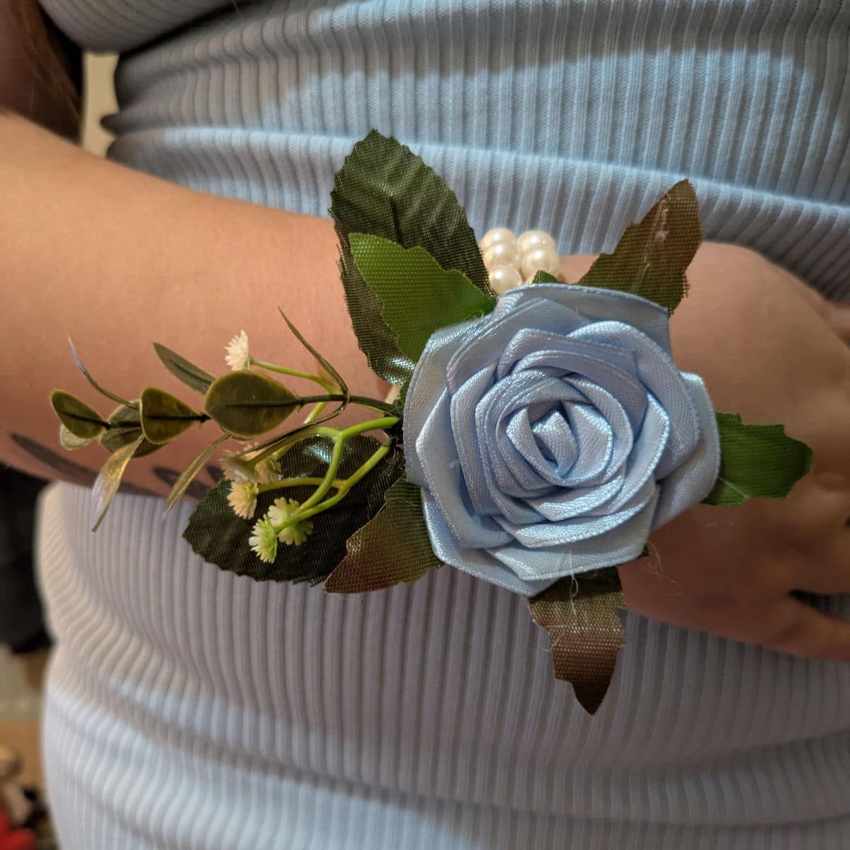 Bluebird satin rose wrist corsage worn on wrist with pearl bracelet and decorative greenery
