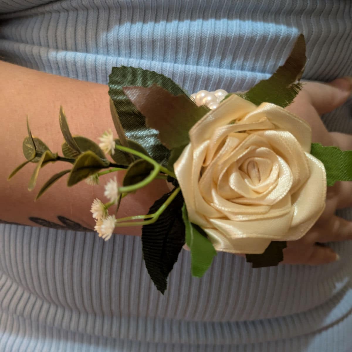 Cream satin rose wrist corsage worn on wrist with pearl bracelet and decorative greenery