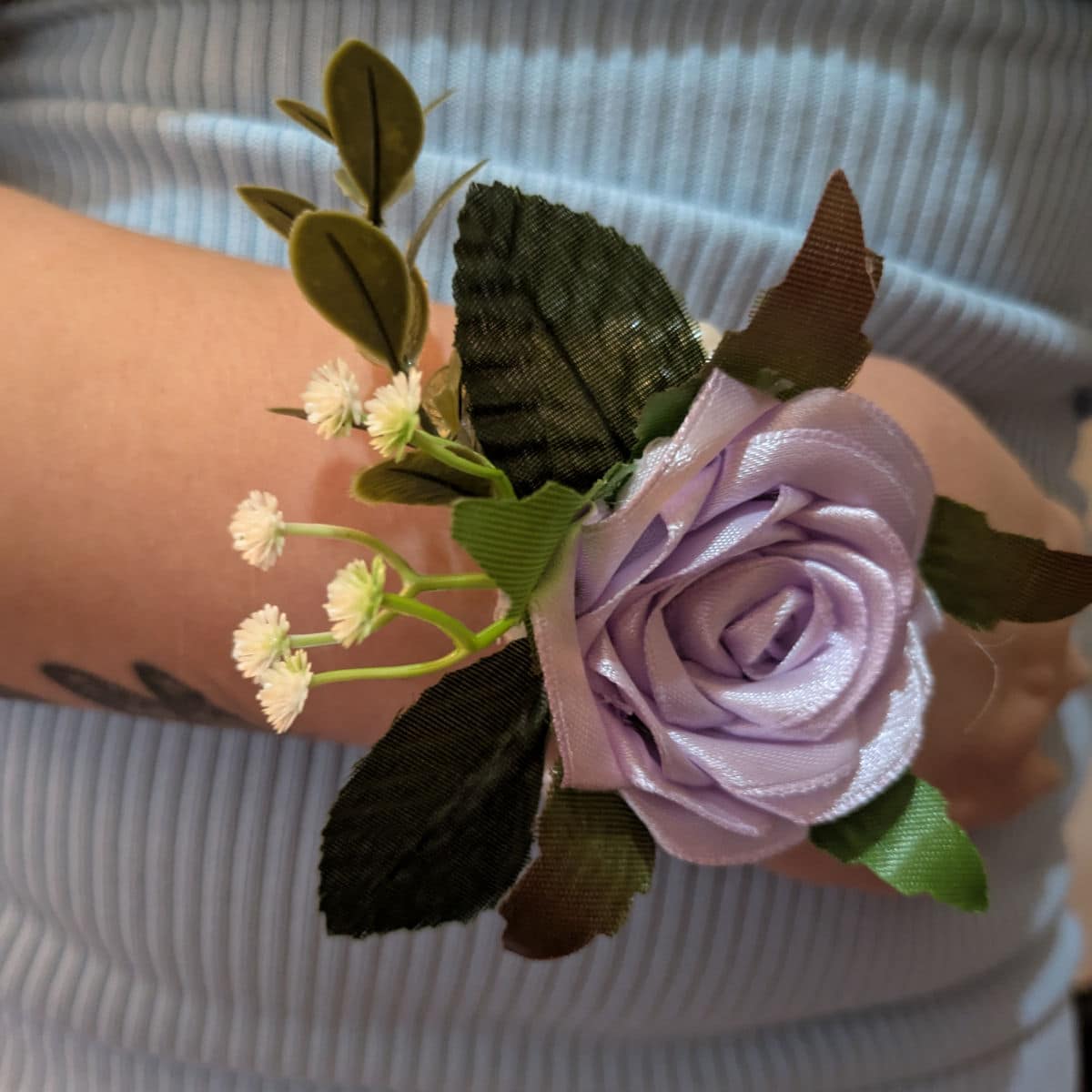 Light orchid satin rose wrist corsage worn on wrist with pearl wristband and decorative greenery