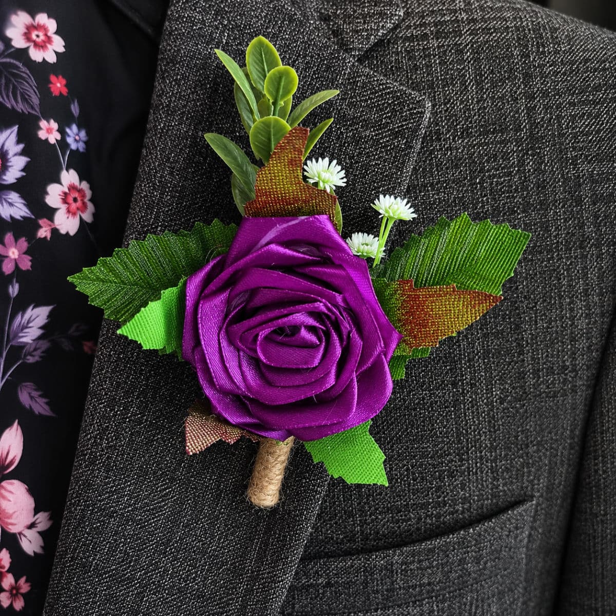 Purple satin rose buttonhole attached to a formal grey suit jacket lapel