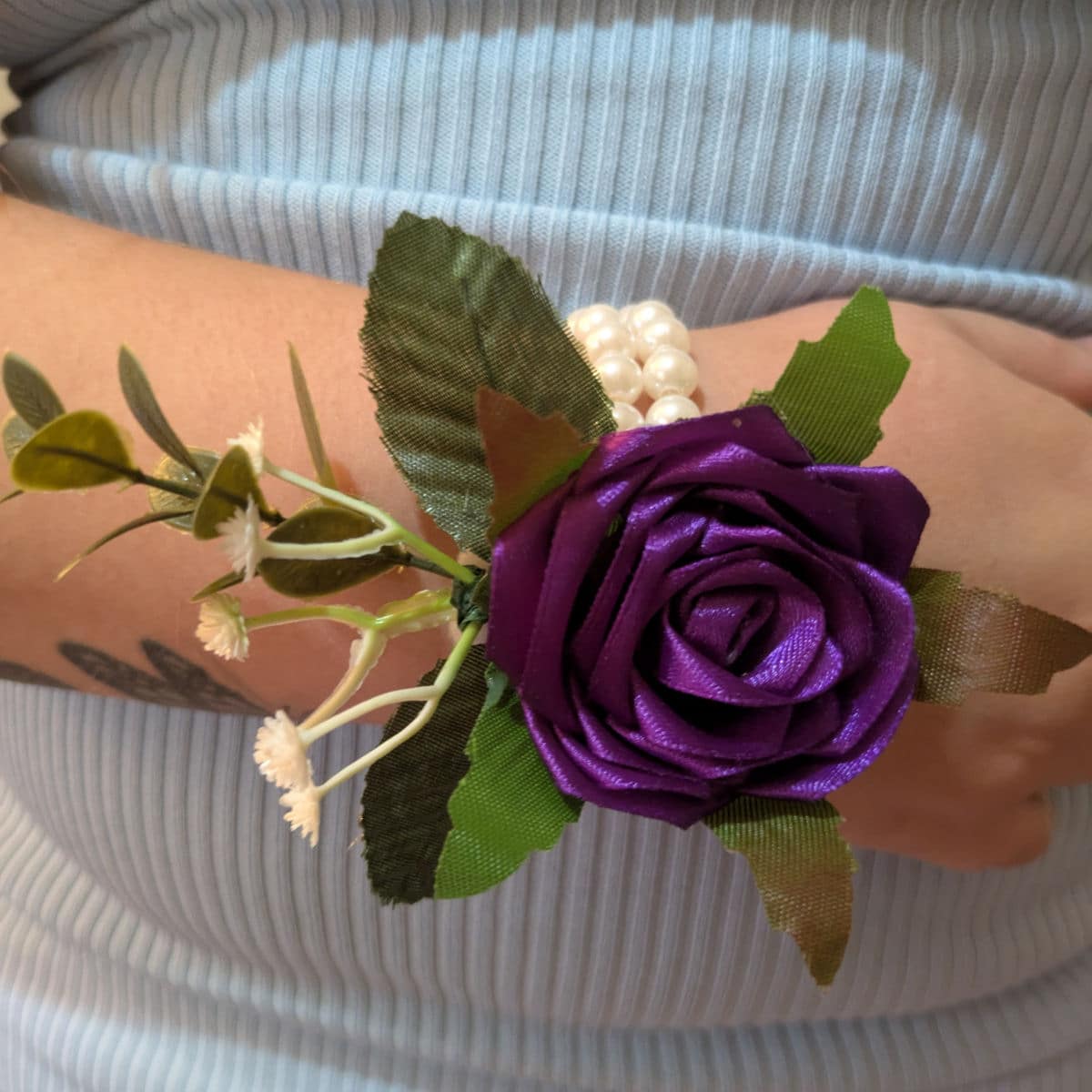Purple satin rose wrist corsage worn on wrist with pearl wristband and decorative greenery