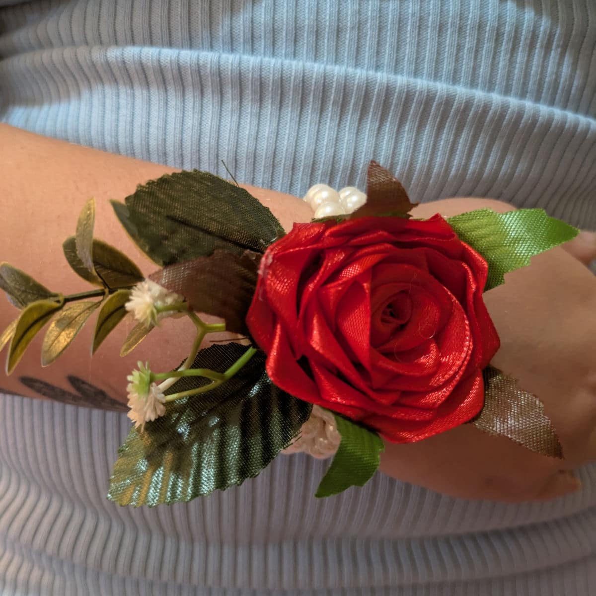 Red satin rose wrist corsage worn on wrist with pearl bracelet and decorative greenery
