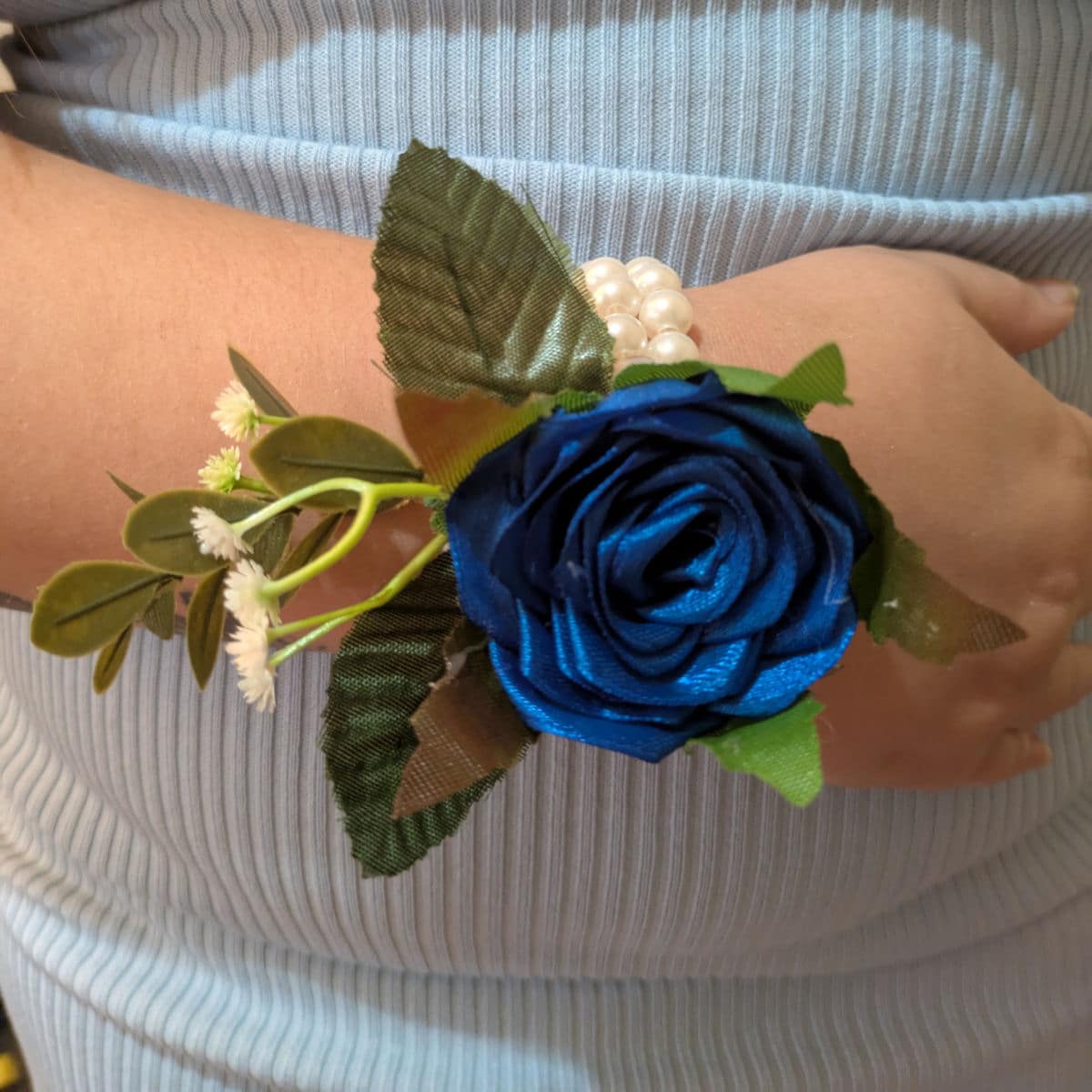 Royal blue satin rose wrist corsage worn on wrist with pearl bracelet and decorative greenery